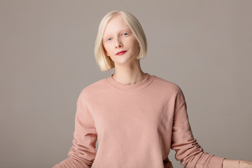 smiling attractive girl in pink stylish sweater isolated on the grey background, close up photo.