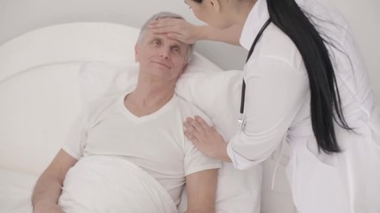 Charming doctor takes care of a disabled senior man in bed