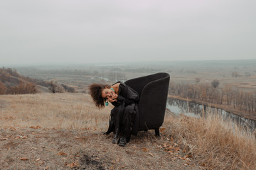 Beautiful girl with curly hair in a stylish suit walks against the backdrop of a beautiful landscape