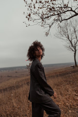 Beautiful girl with curly hair in a stylish suit walks against the backdrop of a beautiful landscape