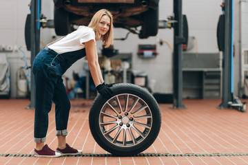 Fototapeta na wymiar attractive blond girl with a wheel looking at the camera in the repair shop. full length photo. lifestyle. girl repairing a car