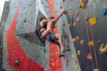 Naklejka na ściany i meble young awesome couple doing aerobic exercise at climbing gym. full length photo. climbing technique, difficulties in climbing
