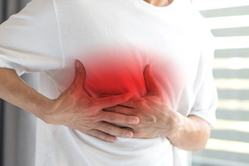 Man's hands on his chest in white shirt with red spot as suffering on chest pain. Male suffer from...