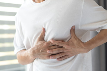 Man's hands on his chest in white shirt with red spot as suffering on chest pain. Male suffer from...