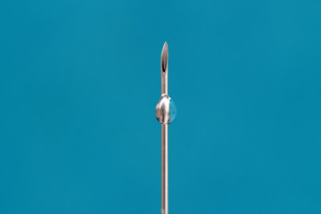needle of a medical syringe with medicine on a blue background