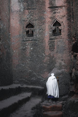 Old priest in white robe praying at a wall at the lalibela church in ethiopia 