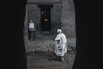 Old priest in white robe with walking stick praying at the  lalibela church in ethiopia 