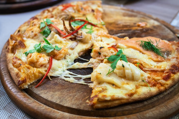 Salmon pizza half with spicy seafood. Fusion Thai style food on wooden pizza serving board at Italian restaurant.