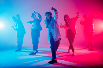 Group of diverse young hip-hop dancers in studio with special lighting effects in blue and pink colores