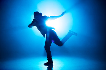 A dark silhouette of a singer on the stage, dancing alone during performance on dark blue neon...