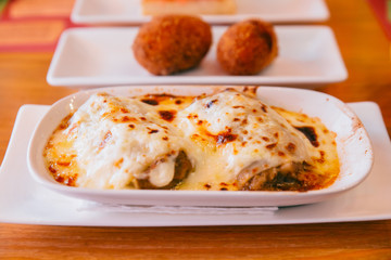 Hot served Lasagne in white plate with Papas Rellenas in background. Spanish and Latin America dish.