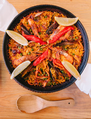 Top view of Paella is including short grain rice, broad bean, prawns, perna viridis and clams, Served with sliced lemons. 