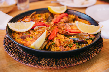 Top view of Paella is including short grain rice, broad bean, prawns, perna viridis and clams, Served with sliced lemons. 