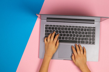 Kid hands typing on laptop computer keyboard, top view, pink and blue background