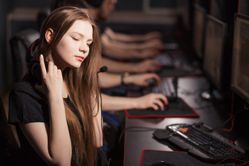 Beautiful female gamer wearing headset, playing in online video game with another people sitting in...