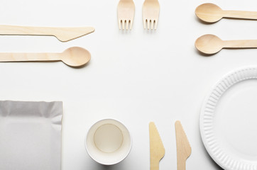Wooden single use kitchenware and paper cups and plates on white. Top view