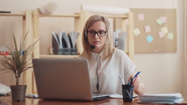 girl Caucasian appearance sitting at the laptop leads the dialogue on the headset on the head and writes the words of the interlocutor
