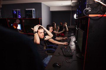 Young female and male gamers playing video game while spending weekend leisuretime at pc gaming club, focused serious people behind pc monitor at dark room. Entertainment or addiction concept