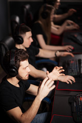 Young female and male gamers playing video game while spending weekend leisuretime at pc gaming club, focused serious people behind pc monitor at dark room. Entertainment or addiction concept