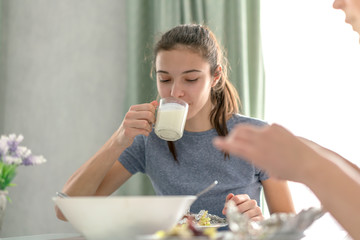 teen girl drinks milk from a glass cup while eating