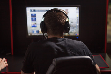 Professional Gamer participating in online cyber games tournament, sitting at pc gaming club or in internet cafe, back view.
