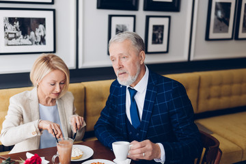 serious grey haired man having breakfast with his wife at the cafe. puzzled man thinking about his family business, free time