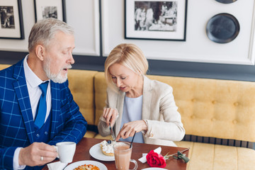 mature couple tasting yummy cake. close up photo. man and woman in stylish suits enjoying the dessert