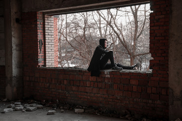 Sad reflective teenager sitting on the windowsill in an unfinished abandoned building, the concept of sadness, depression in young people