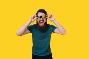 Excited young bearded man wearing futuristic glasses looking at the camera on yellow background.