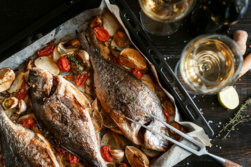 dinner concept for two. two glasses of white wine, baked fish.