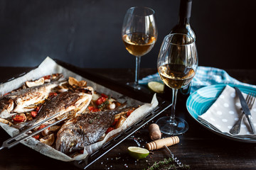 dinner concept for two. two glasses of white wine, baked fish.