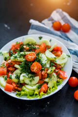 Fresh spring vegetable salad from tomato and cucumber on a black background, close up.