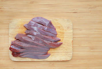Raw fresh sliced pork liver on wooden board background.