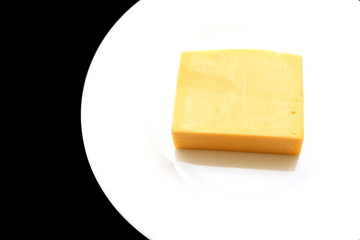 Closeup of a piece of cheese on a white plate on a black background. Natural dairy products, delicious food
