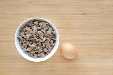 Chopped of boiled pork liver in white bowls on wooden board with egg.
