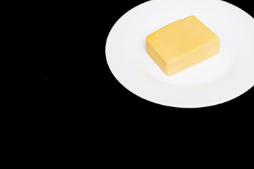 Closeup of a piece of cheese on a white plate on a black background with copy space. Natural dairy products, delicious food