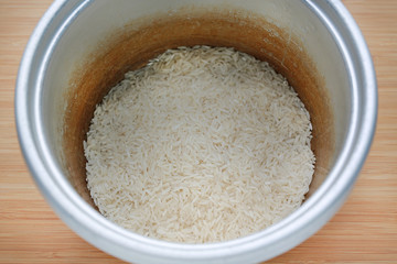 Raw Thai local jasmine rice in pot on wood background ready for cooking.