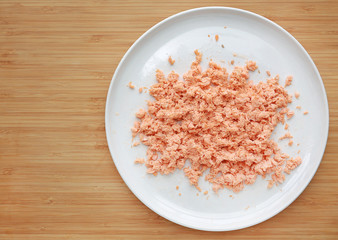 Shredded salmon fish in white plate on wooden board background with copy space.