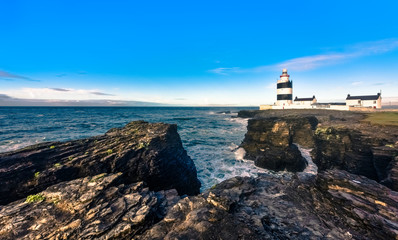 Scenic Hook Lighthouse on rugged cliffs with blue sky, Country Wexford, Ireland