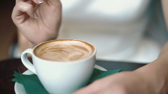 Girl stirs coffee with spoon, dripping drops, close-up, slow motion