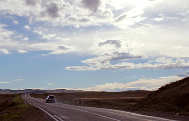 road in steppe under a blue sky with white clouds Sayan mountains Siberia Russia