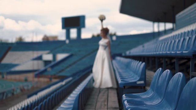 Young beautiful bride, defocused, stands in the stadium and is happy for her favorite team, in the hands she has a bouquet of flowers