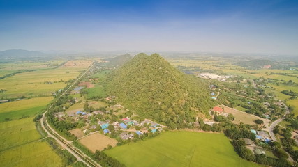 Obraz premium Aerial view above green rice fields plantations with small hill with blue sky background, khao Phra - khao Noi, Thamaka District, Kanchanaburi, Thailand.