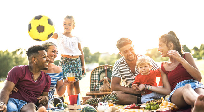 Happy multiracial families having fun together with kids at pic nic barbecue party - Multicultural joy and love concept with mixed race people playing with children at park - Warm contrasted filter