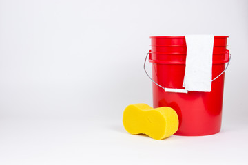 Red bucket with wash cloth and sponge on white background.