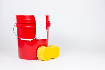 Red bucket with wash cloth and sponge on white background.