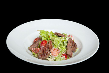 Veal salad, salad with large slices of veal and fresh vegetables on a plate on a black background