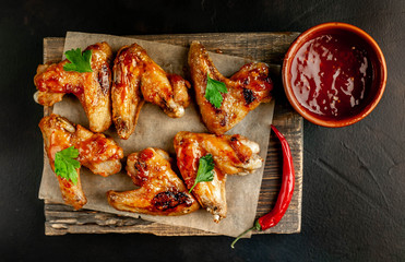 Grilled chicken wings in a barbecue sauce with parsley on a cutting board on a concrete table.