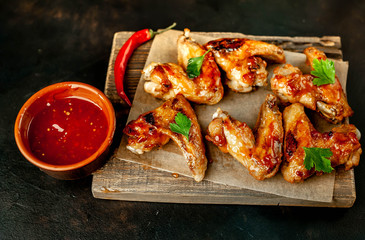 Grilled chicken wings in a barbecue sauce with parsley on a cutting board on a concrete table.