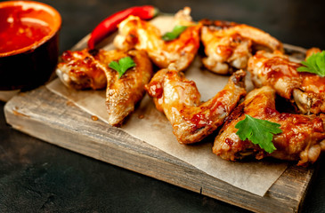 Grilled chicken wings in a barbecue sauce with parsley on a cutting board on a concrete table.